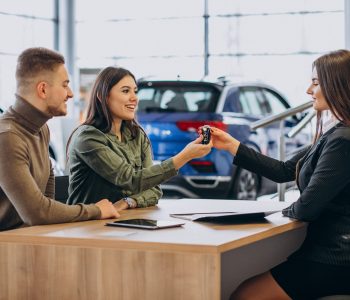 Young couple talking to a sales person in a car showroom about financing and Credit Scores for a vehicle loan.
