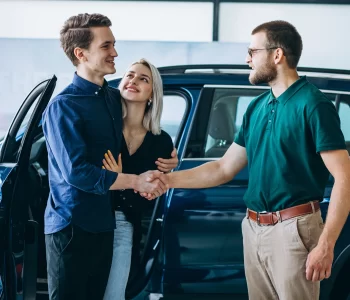 Couple shaking hands with a car salesperson next to a vehicle, illustrating when to Purchase a Car in Australia.