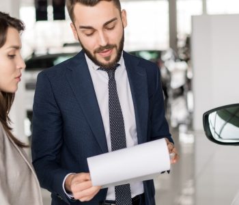 Customer reviewing documents with a car dealer during the lease-to-own car approval process at a dealership.