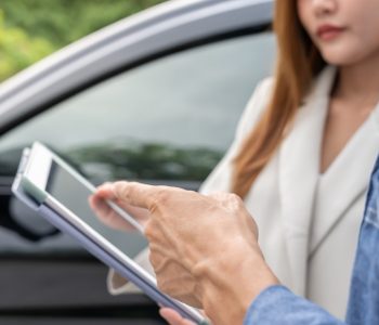 Person reviewing details of a car subscription fee on a tablet while standing beside a vehicle