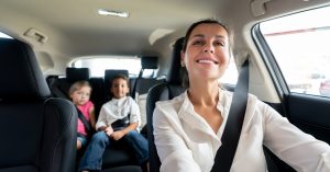 Mother driving a family car with two children in the back seat, representing Australians looking for more stable car finance options during rising interest rates.