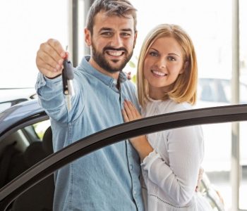First-Time Car Buyers receiving car keys from a dealership while standing beside their newly purchased vehicle.